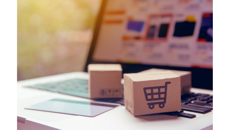 Aufgeklappter Laptop mit Kreditkarte und Holzwürfel auf dem ein Einkaufswagen abgebildet ist